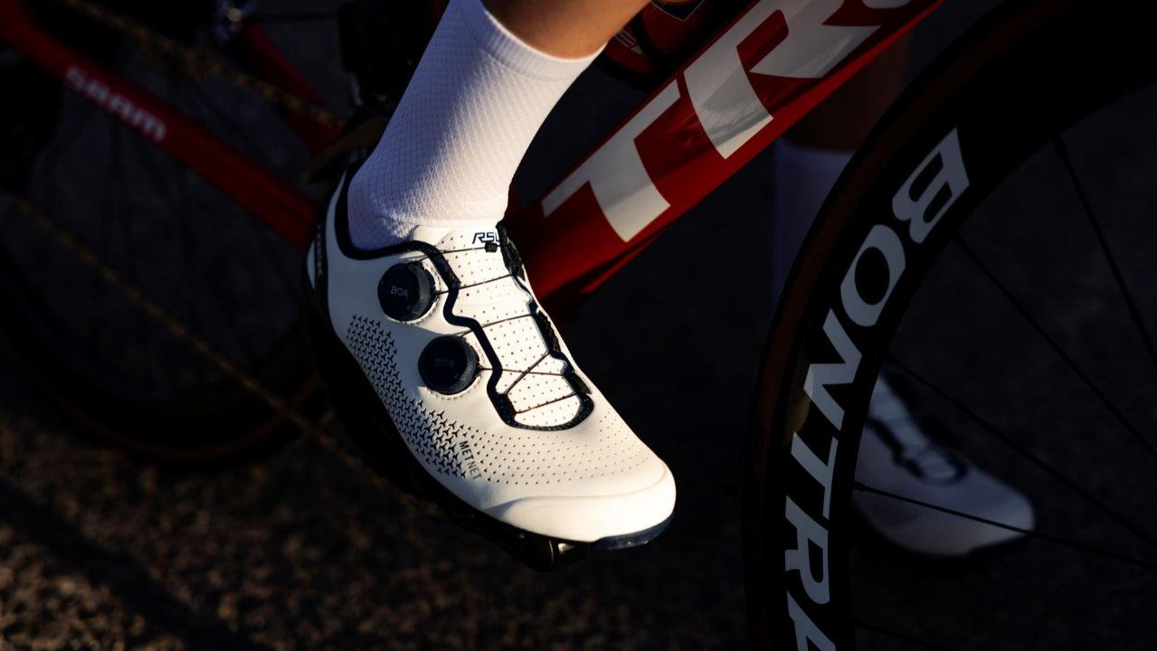 Cycling shoe with white sock and bicycle wheel in the background