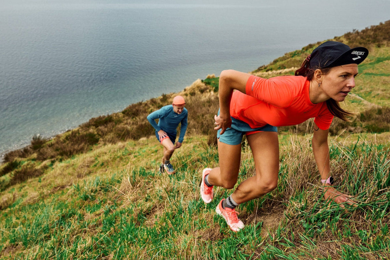 Two runners on a grassy hill with a scenic ocean view