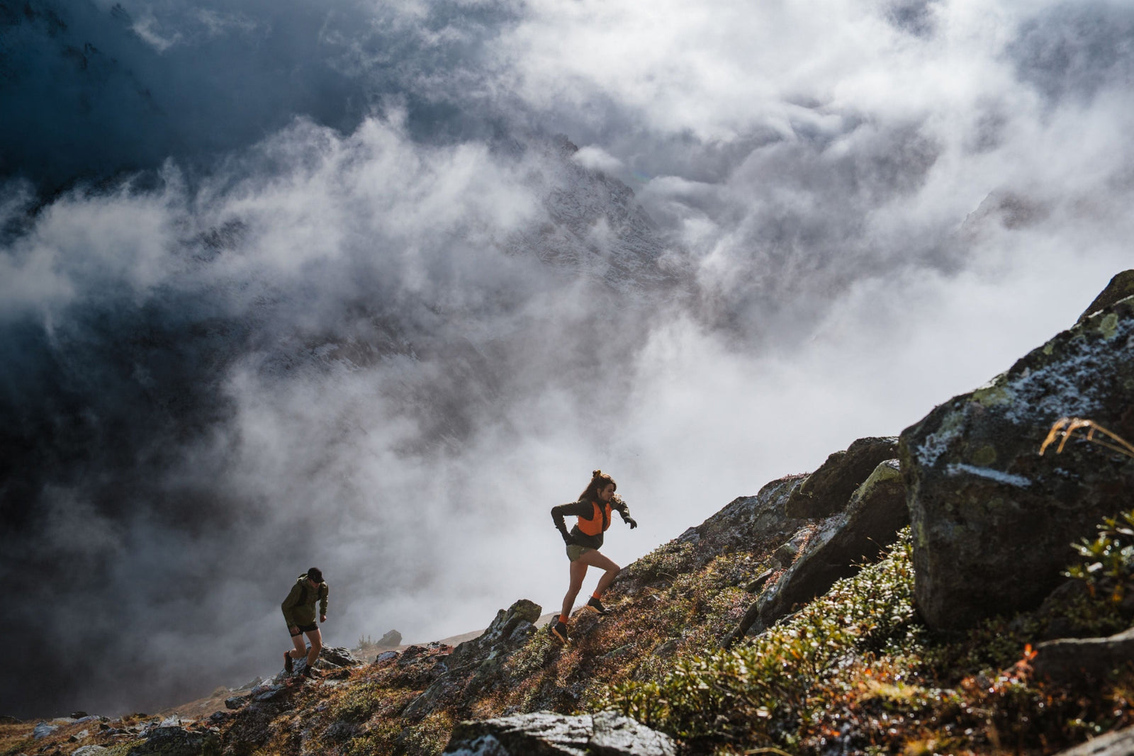 Two people hiking on a mountain trail with clouds in the background