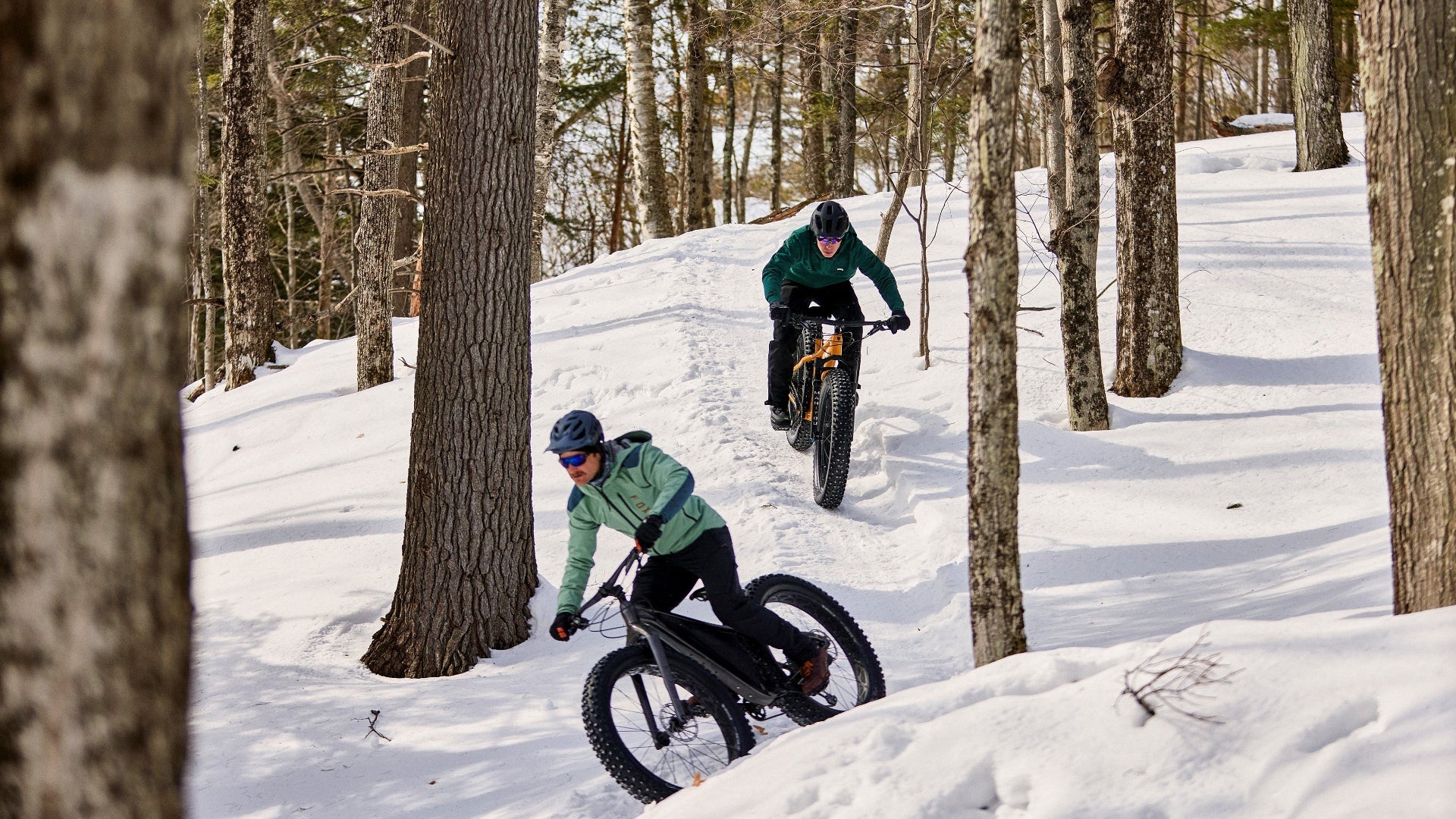 Two people riding fatbikes through a snowy forest.