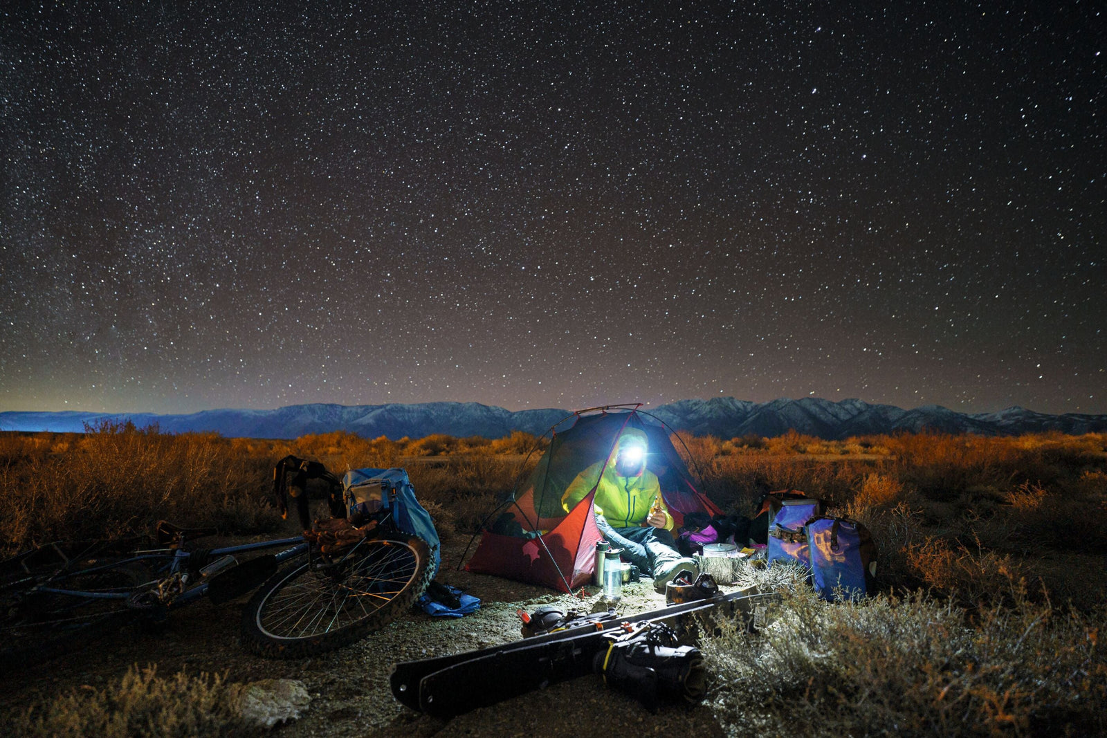 Camping scene under a starry sky with a tent, person, and bicycle.