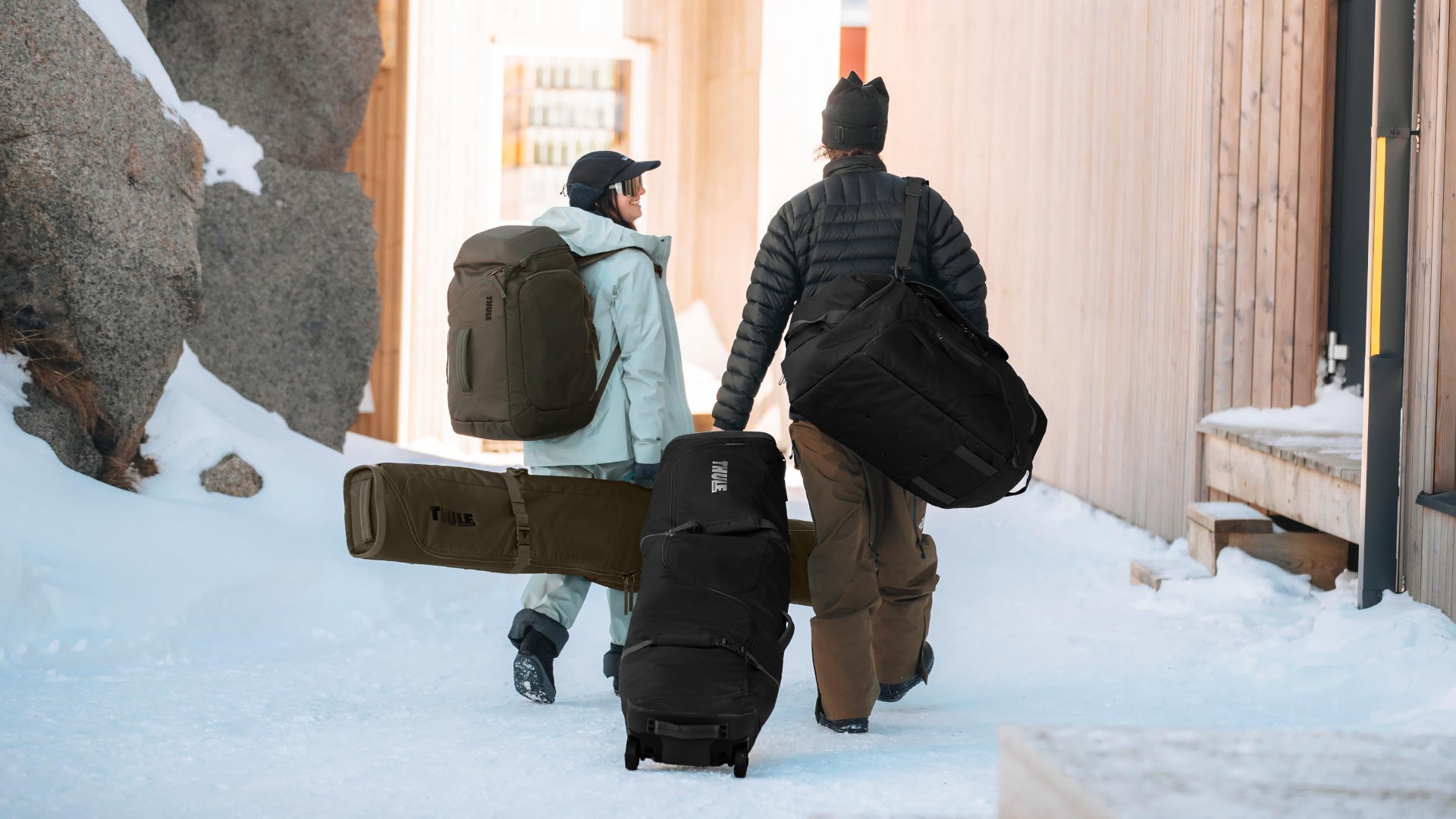 Two people walking in the snow with ski bags.