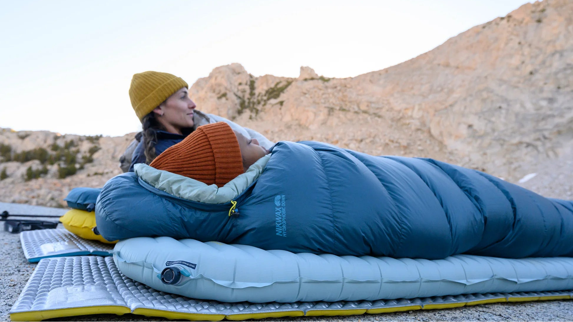 Person lying in a blue sleeping bag on a sleeping pad in a mountainous area