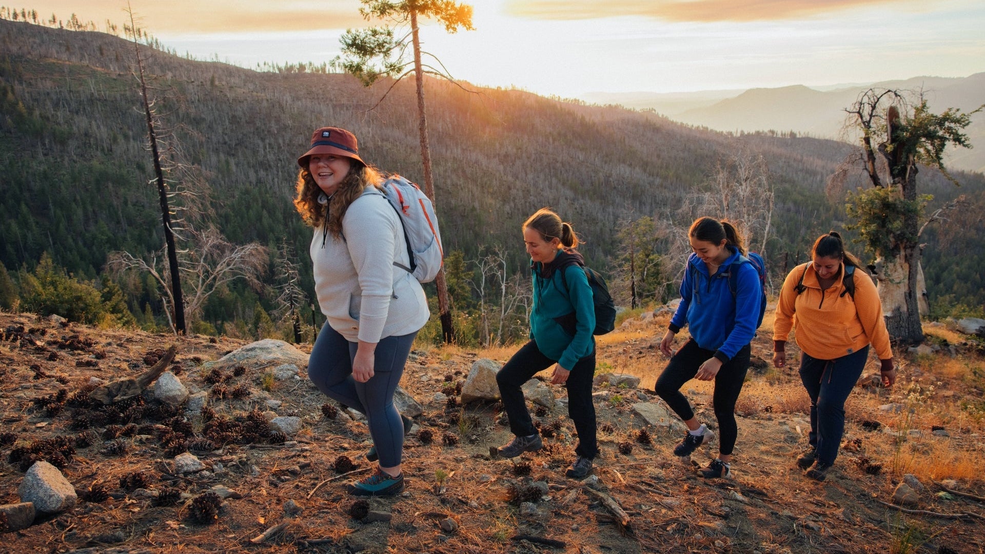 Four people hiking on a mountain trail with a scenic sunset background